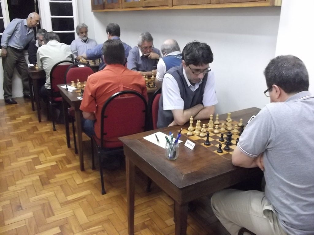Mais dez enxadristas nas cinco mesas à direita. Paschoal Mendes ao fundo.