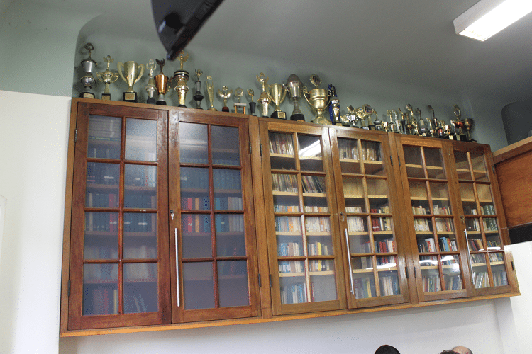 A estante da Biblioteca Dijalma Caiafa e a coleção de Troféus conquistados pelo clube